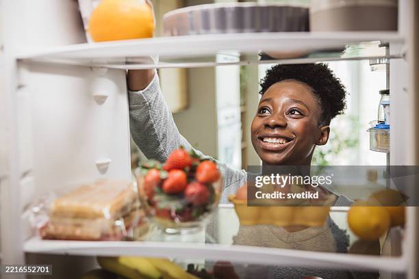 frau, die lebensmittel aus dem kühlschrank voll mit lebensmittel - lagerhaltung stock-fotos und bilder