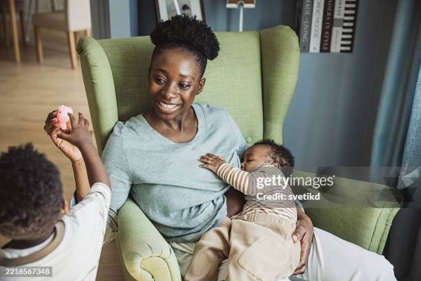 young mother breastfeeding baby while playing with toddler - mid adult women stock pictures, royalty-free photos & images