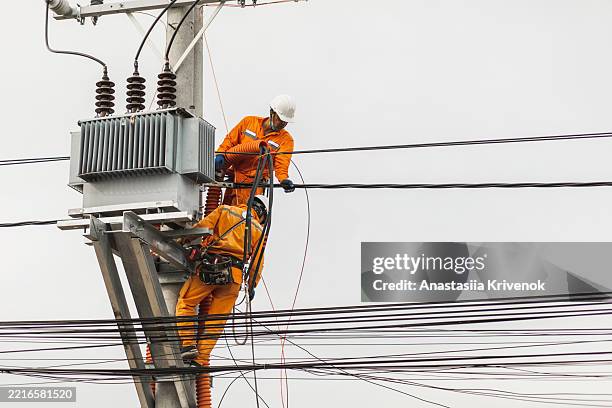 electrical workers maintaining power lines on high utility pole - rede elétrica imagens e fotografias de stock