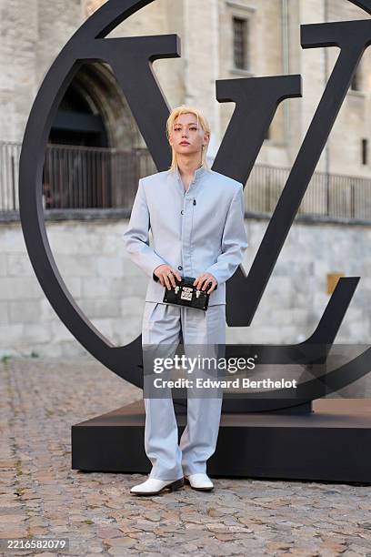 Felix wears a light gray tailored suit featuring a structured blazer with a high collar and button detailing, paired with matching wide-leg trousers....