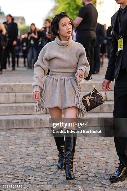 Moeka Hoshi wears a beige turtleneck sweater dress with fringe detailing at the hem, paired with knee-high black leather boots. A brown Louis Vuitton...