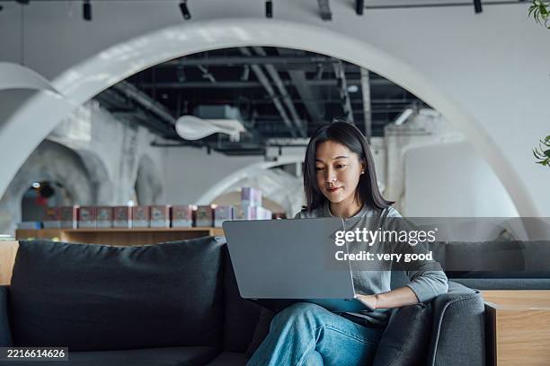 joven mujer asiática trabajando en una computadora portátil mientras está sentada en el vestíbulo de la oficina - fundador fotografías e imágenes de stock