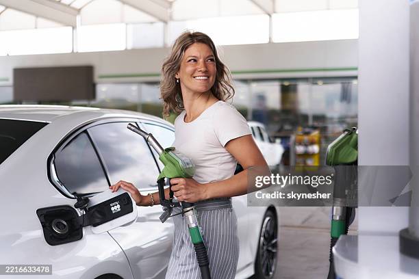 sorglose frau, die gerade dabei ist, ihren autotank an der tankstelle zu tanken. - tanken stock-fotos und bilder