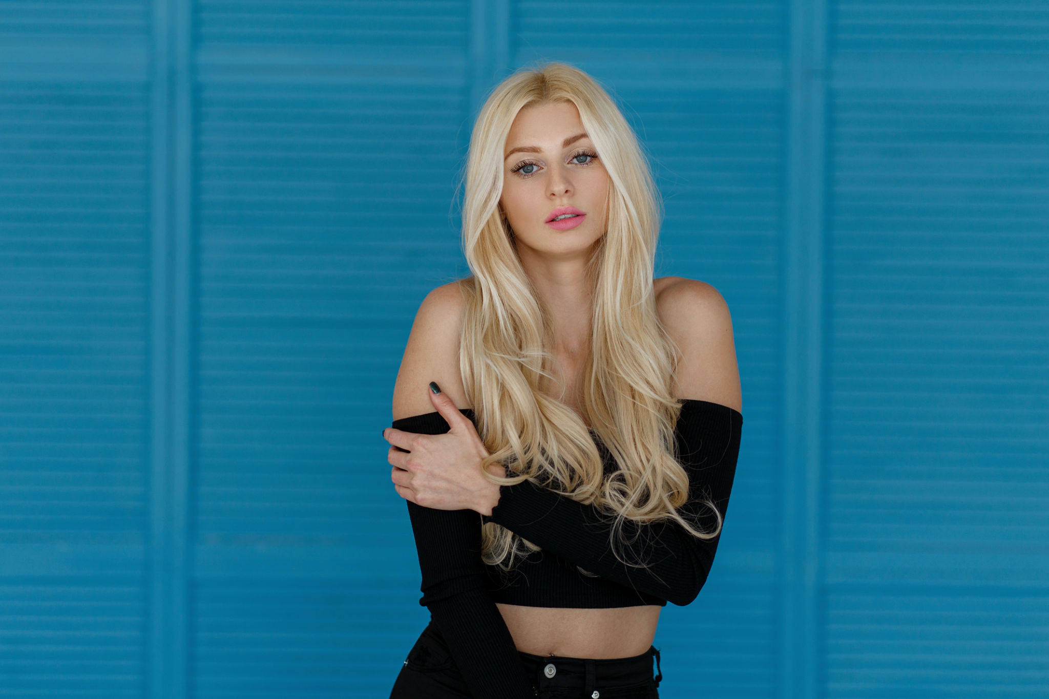 Pretty young stylish model woman with freckles with pink lips and long blond hair posing in the studio near a wooden blue wall Pretty young stylish model woman with freckles with pink lips and long blond hair posing in the studio near a wooden blue wall