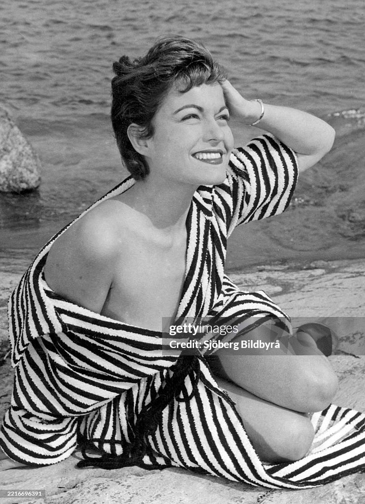 1950s summer. A young woman wearing a stripe patterned bathrobe on the beach a sunny summer's day. Pho...