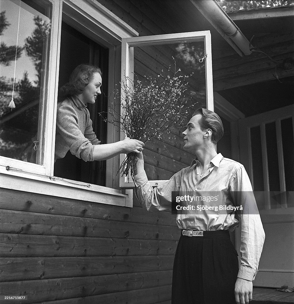 Lifestyle in the 1950s. A young couple pictured at their house. He is handing her a bouquet of branche...