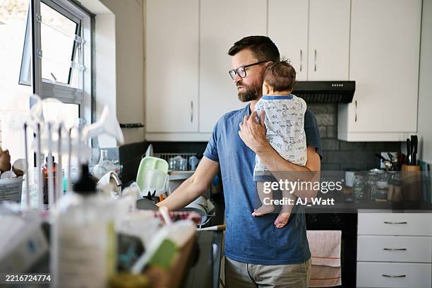 father holding his baby while looking at dirty dishes in the kitchen sink - imperfection stock pictures, royalty-free photos & images