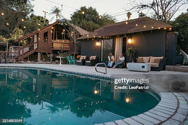 due donne in vacanza godendo di una bella serata con un drink a bordo piscina della loro casa in affitto - casa in affitto foto e immagini stock