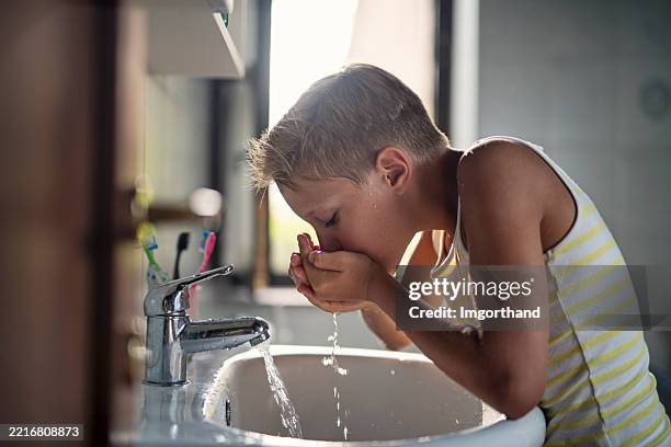 glücklicher kleiner junge, der sich unter fließendem wasser in einem waschbecken die hände wäscht - fließendes wasser stock-fotos und bilder