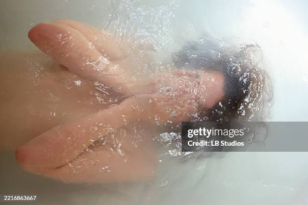 woman submerged in water with face and hands visible through bubbles and ripples - water reflection face stock pictures, royalty-free photos & images