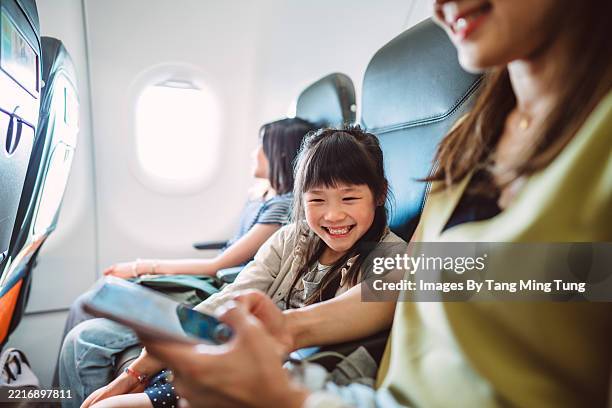 mother and daughter using smart phone together on airplane during travelling - family excitement stock pictures, royalty-free photos & images