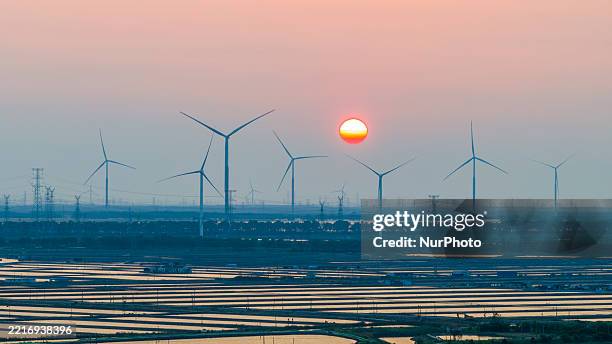 Wind turbines above photovoltaic panels operate at the tidal flat industry demonstration base in Yancheng City, Jiangsu Province, China, on May 28,...