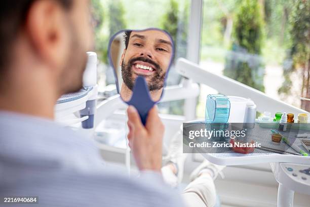 giovane felice che tiene lo specchio ammirando il sorriso dopo il trattamento dentale - sbiancamento dentale foto e immagini stock
