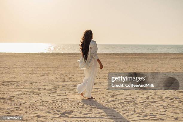 mujer caminando en una playa durante la puesta del sol en un entorno tranquilo - una sola mujer joven fotografías e imágenes de stock