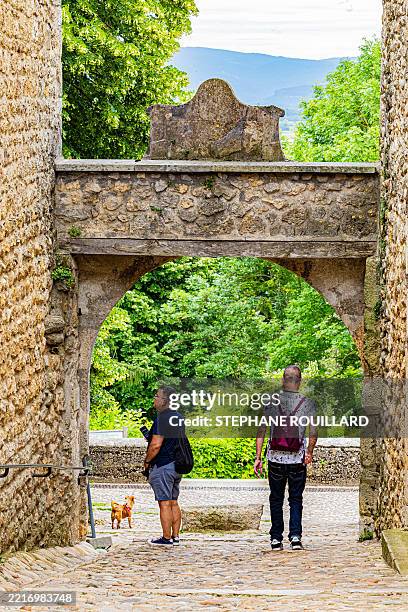 Two men and a dog exit through the lower gate of the medieval city of Perouges in the Ain department of France on May 28, 2025.