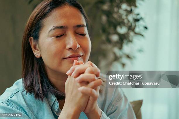 close-up face woman sits and prays on a sofa. - praying stock pictures, royalty-free photos & images