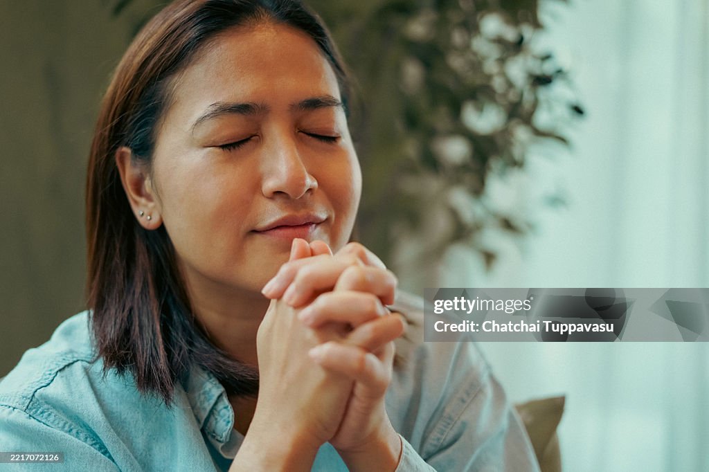 Close-up face woman sits and prays on a sofa.