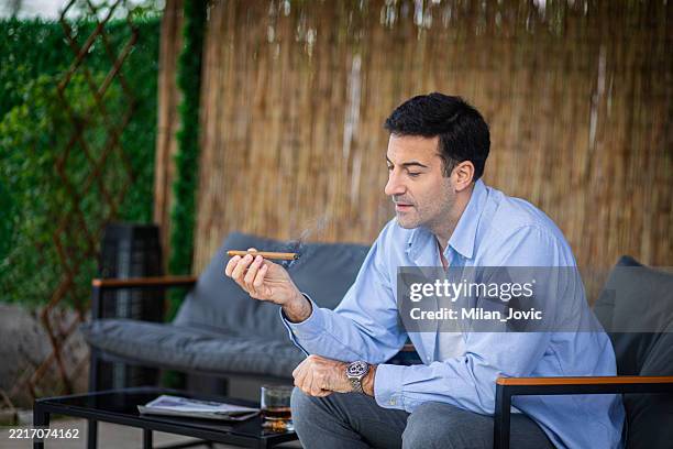 elegant man smoking a cigar on an outdoor patio - elegant smokers stock pictures, royalty-free photos & images