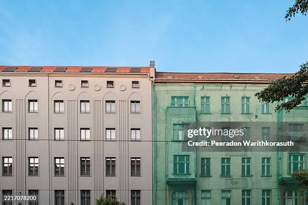 a freshly renovated building with smooth, modern detailing and an adjacent older structure covered in green construction netting. - capital cities stock pictures, royalty-free photos & images