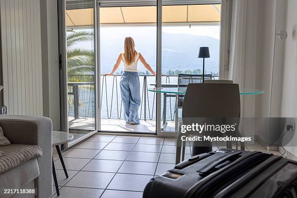 entspannte frau, die ihr gepäck abstellt und den blick auf den balkon genießt - hotelzimmer stock-fotos und bilder