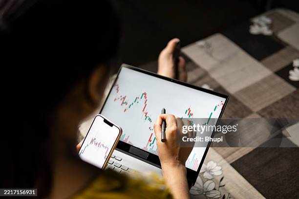 millennial investor young woman analyzing financial trading graph on laptop and smartphone. - over the shoulder view stock pictures, royalty-free photos & images