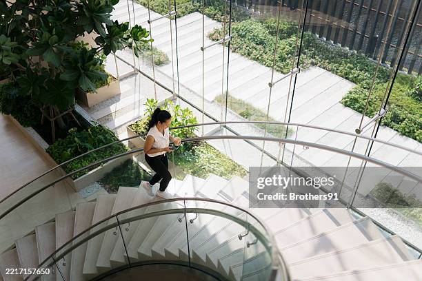 businesswoman walking down stairs in modern office building with coffee and smartphone - trap stockfoto's en -beelden