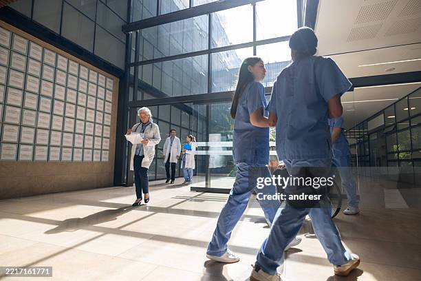 healthcare workers walking through an entrance hall at a hospital - hospital stock pictures, royalty-free photos & images