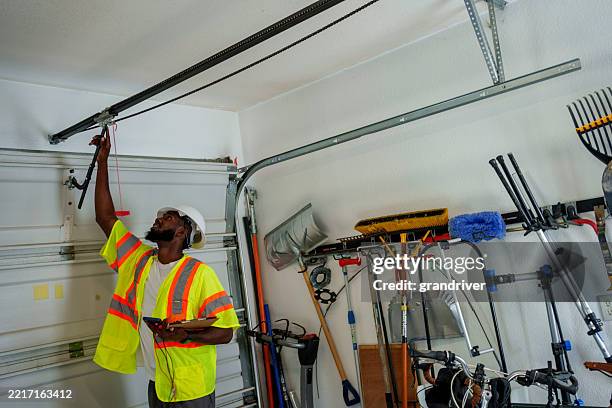 young african american home inspector examining a garage door opener in a residential garage - deur stockfoto's en -beelden
