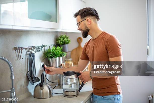 joven enchufando una tetera eléctrica en una cocina moderna - enchufar fotografías e imágenes de stock