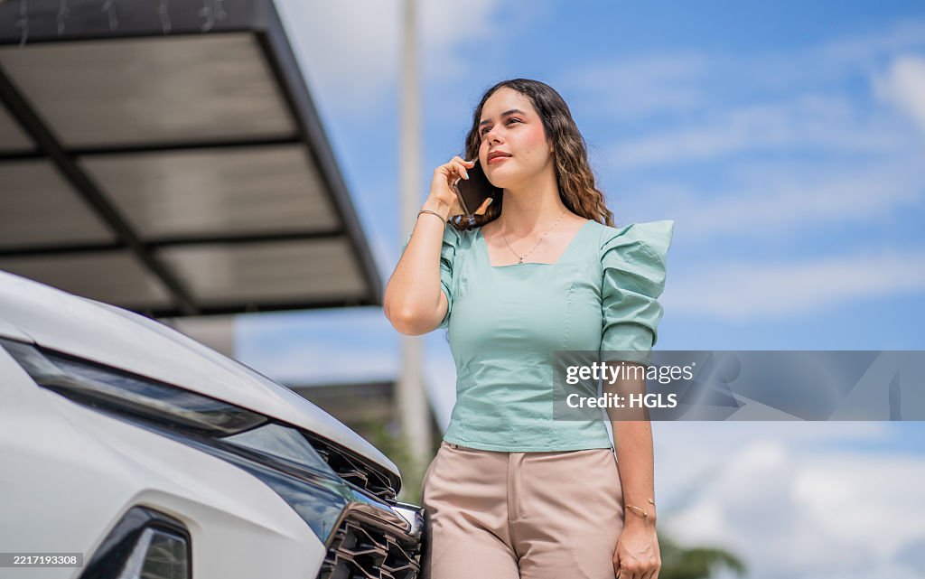 Young professional young woman talking on phone outdoors next to her modern car.