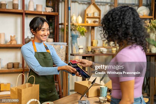 woman paying with credit card in ceramic shop smiling at salesperson - credit card art stock pictures, royalty-free photos & images