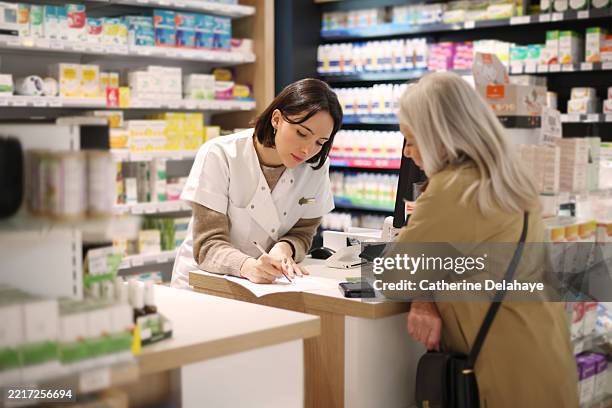 a female pharmacist discussing a prescription with an elderly lady customer at the service counter in a pharmacy. - bâtiment public photos et images de collection