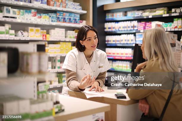 a female pharmacist discussing a prescription with an elderly lady customer at the service counter in a pharmacy. - farmacia fotografías e imágenes de stock