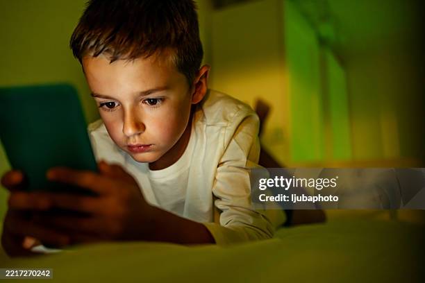 young boy focusing on smartphone screen in cozy evening lighting - staring at screen stock pictures, royalty-free photos & images