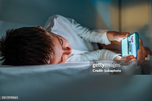 young boy using smartphone in bed during nighttime - using phone screen stock pictures, royalty-free photos & images
