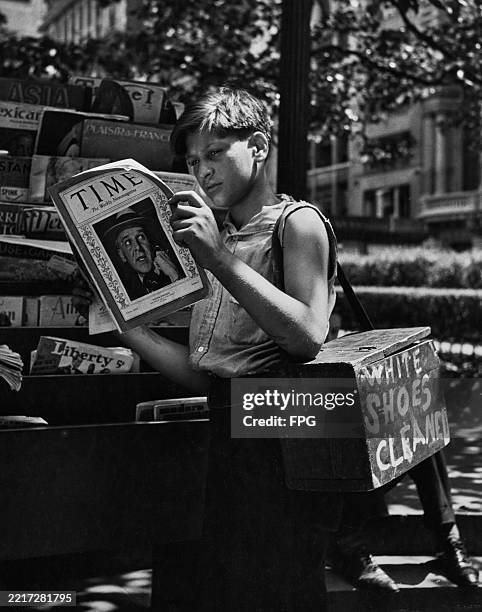 Boy carrying a shoe shine box over his shoulder and reading a copy of 'Time' magazine, July 1938. American newspaper gossip columnist Walter Winchell...