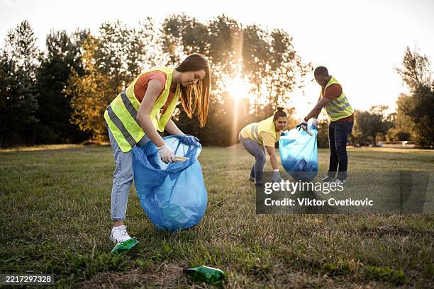 volunteers picking up trash in a public park during sunset - sanitation worker stock pictures, royalty-free photos & images