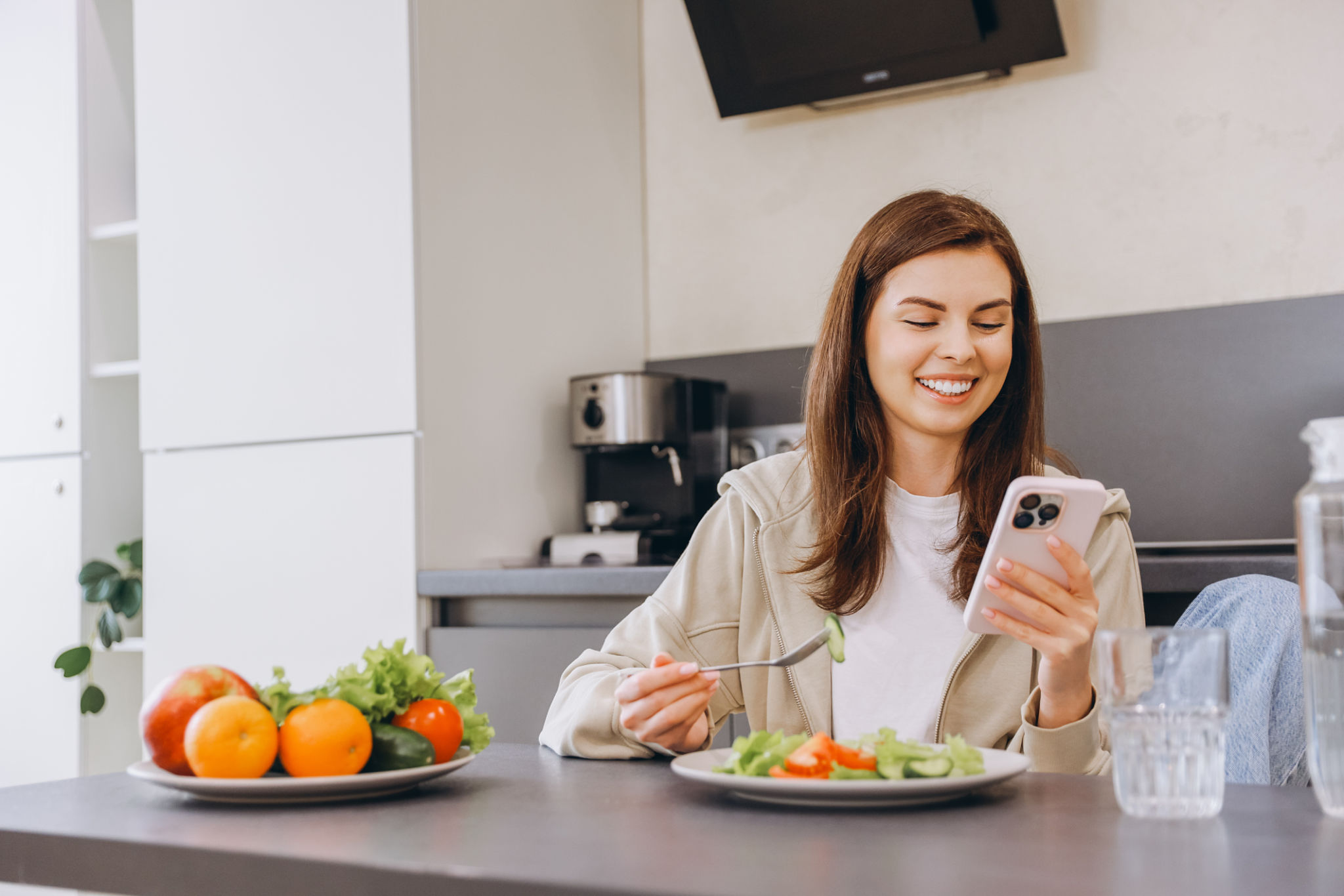 Woman enjoying healthy meal and using smartphone in modern kitchen Woman enjoying healthy meal and using smartphone in modern kitchen