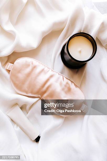 a silk sleep mask and an open candle jar placed on white fabric - kuuroord stockfoto's en -beelden