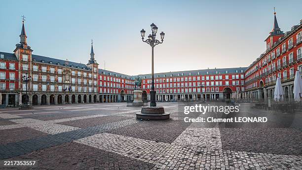 panorama of the plaza mayor square of madrid at sunrise, with a view on the casa de la panaderia (panadería), the casa de la carniceria, the bronze statue of philip iii, empty cafe terraces and red facades, los austrias - community of madrid - spain. - empty street stock pictures, royalty-free photos & images