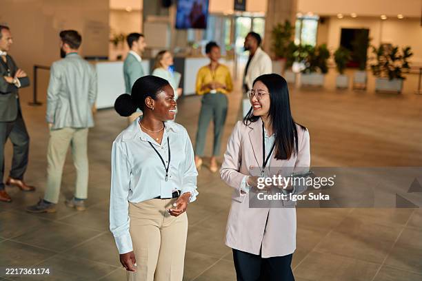 dos mujeres de negocios caminando y hablando en una conferencia - feria comercial fotografías e imágenes de stock