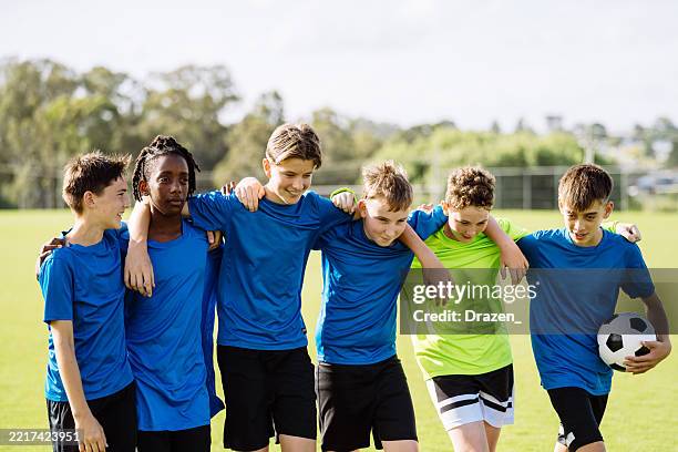 grupo de jugadores de fútbol adolescentes con camisetas azules en un campo verde abrazándose después de marcar un gol - equipo de fútbol fotografías e imágenes de stock
