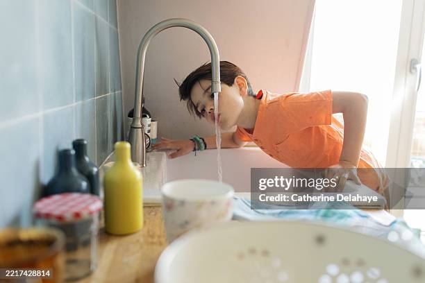 a little boy drinking water from the tap at home - niño-tomando-agua fotografías e imágenes de stock