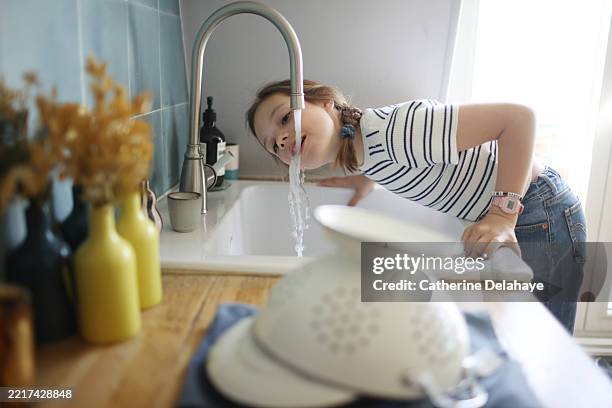 a little girl drinking water from the tap at home - niño-tomando-agua fotografías e imágenes de stock