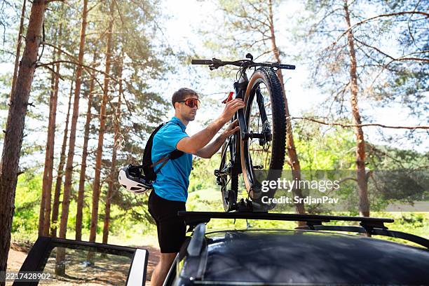 man securing a mountain bike on a car roof in a forest - rack stock pictures, royalty-free photos & images