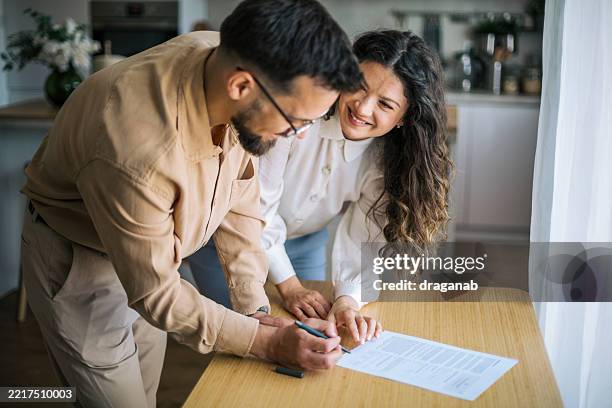 happy couple smiling and reading a contract before signing it at home - tenant stock pictures, royalty-free photos & images