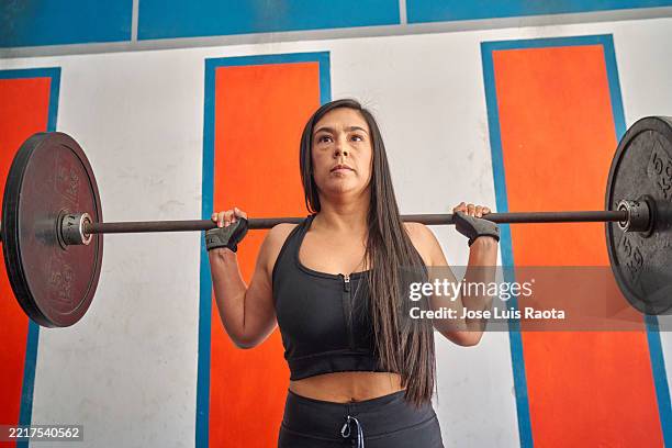 fitness enthusiast woman lifting barbell in well-equipped gymnasium - barbell stock pictures, royalty-free photos & images
