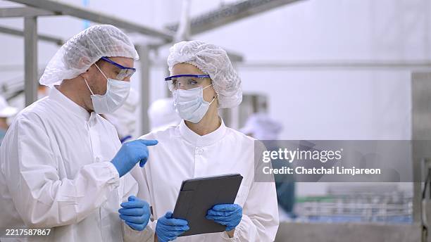 product researcher or quality control engineer or production line worker in white sterile uniforms prevent contamination of food and drink product industry or cosmetic manufacturing plants or processed food or canned food, discuss about product at factory - voedsel-verwerkingsbedrijf stockfoto's en -beelden
