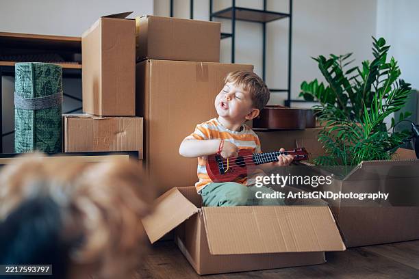 charming boy playing the guitar in a carboard box during a move-in. - musikinstrument bildbanksfoton och bilder