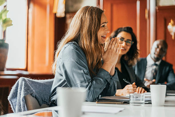 smiling businesswoman with hands clasped communicating with colleagues in meeting room at office - business finance and industry stock pictures, royalty-free photos & images